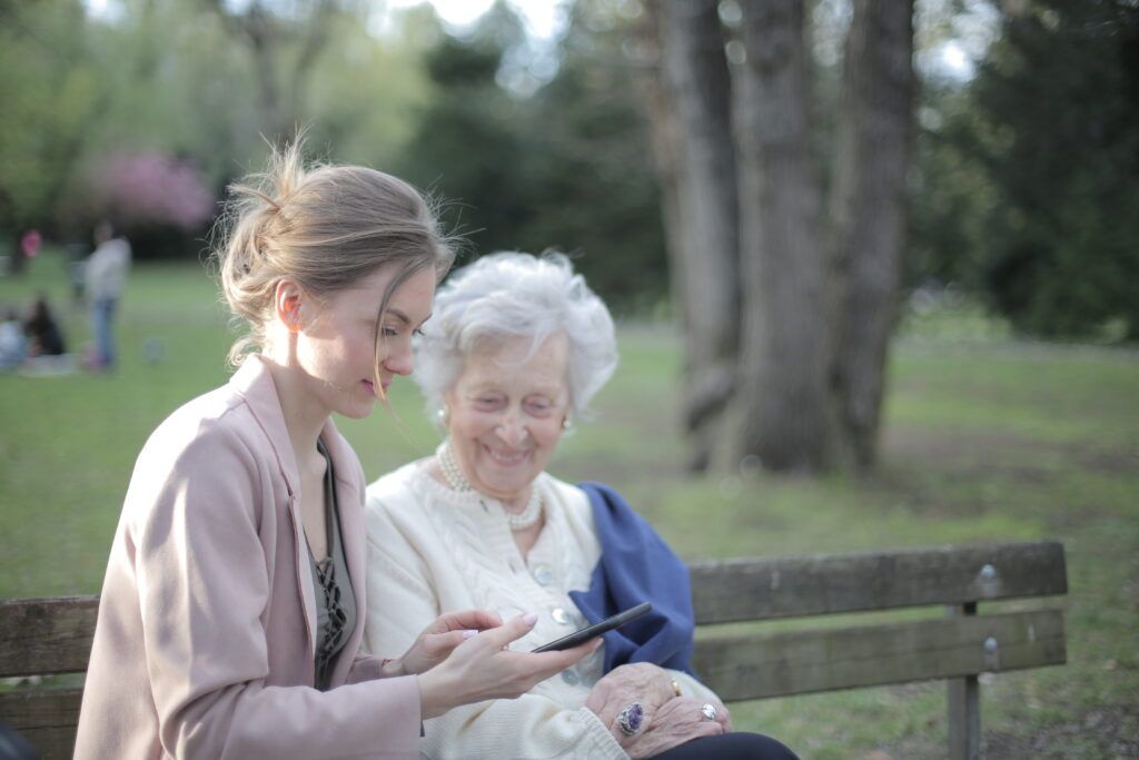 3791666-3791666 Side view of smiling adult female helping aged mom in using of mobile phone while sitting together in park