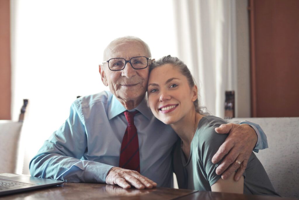 3823497-3823497 Positive senior man in formal wear and eyeglasses hugging with young lady while sitting at table
